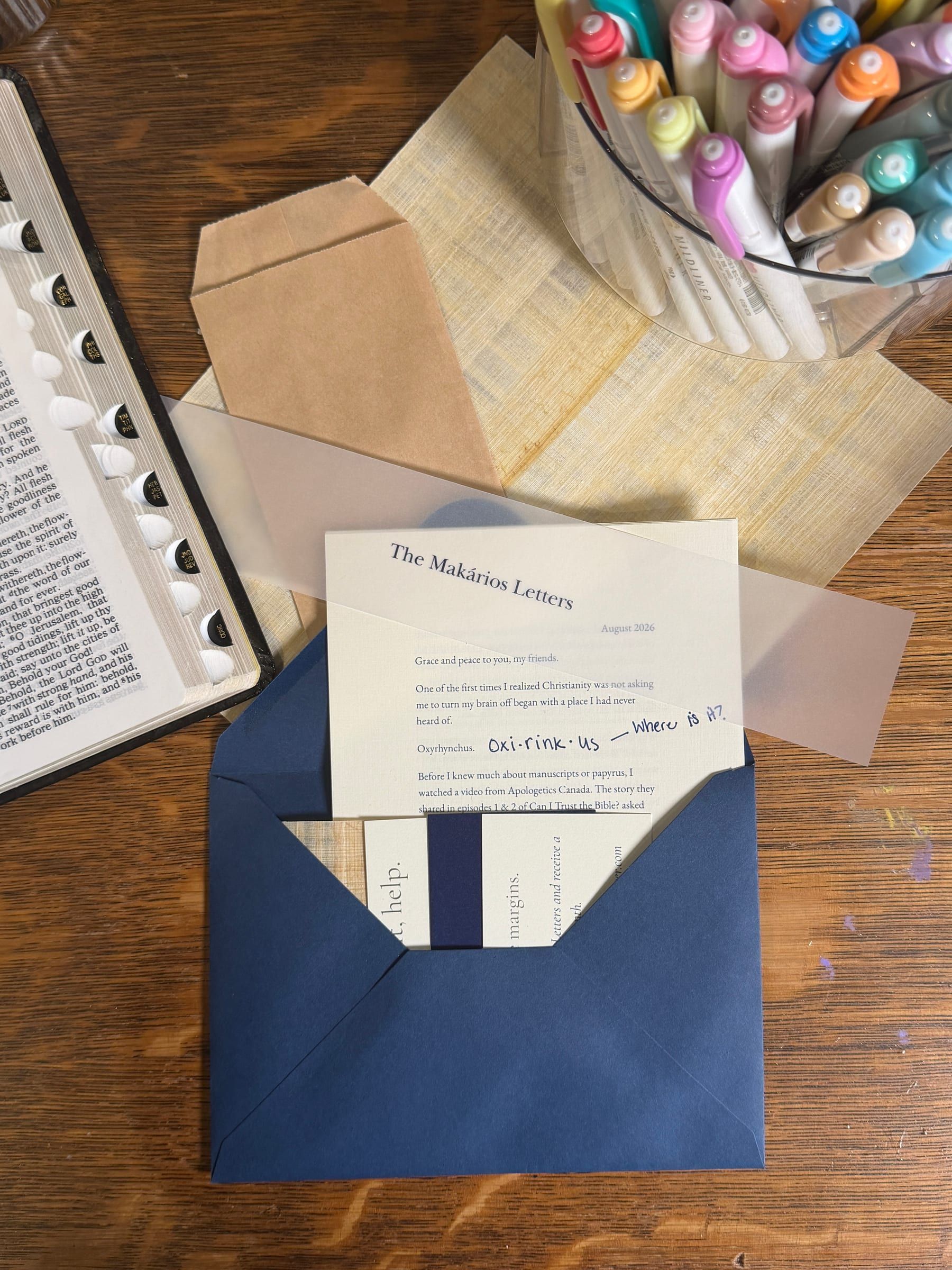 The August 2026 letter rises out of an open navy envelope under a vellum band, with cards behind it and papyrus and pens beyond.